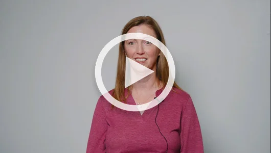 Smiling woman in pink top giving video testimonial with play icon overlay